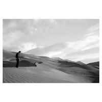 a black and white photograph of a man standing on a sand dune